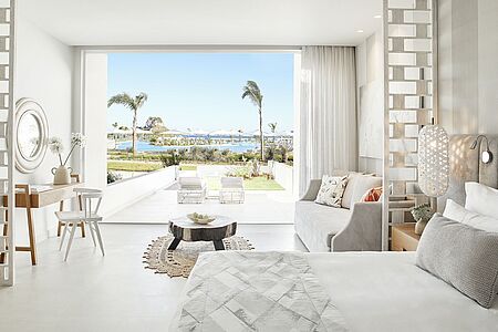 Deluxe Junior Suite mit privatem Garten In diesen geräumigen Suiten mit privatem Garten lässt sich das Leben drinnen und draußen nahtlos miteinander verbinden. Mit ausreichend Platz für zwei Erwachsene und zwei Kinder, bietet jede der ca. 50qm großen Suiten ein Schlafzimmer und Wohnzimmer in einem modernen, offenen Design, abgerundet durch ein Schlafsofa und einen Essbereich. Die bodentiefen Fenster bieten einen herrlichen Blick auf die Gärten, den schönen Lagunenpool oder die Ägäis, während der private Garten viel Platz zum Entspannen bietet.