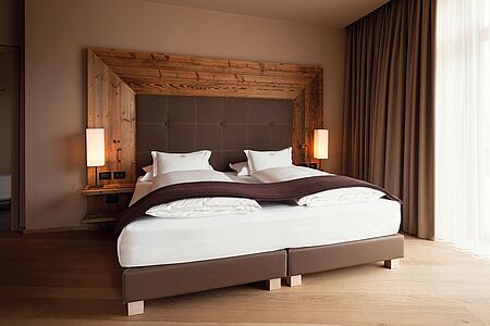 Chalet Deluxe Suite (ca. 75 - 80 qm) Diese Luxussuiten mit großzügigem Balkon und exklusivem Dolomiten-Blick befinden sich im dem Haupthaus gegenüberliegenden Chalet und sind mit diesem durch einen unterirdischen Gang verbunden. Sie sind fächerförmig angelegt und verfügen über ein separates Wohnzimmer mit Bio-Kamin und Esstisch, sowie ein großzügiges Badezimmer mit Doppeldusche und freistehender Badewanne.