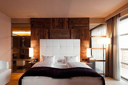 Deluxe Suite (ca. 150 qm) Die Deluxe Suiten für 4 Personen verfügen über zwei separate Schlafzimmer, ein geräumiges Wohnzimmer mit gemütlicher Sitzecke, Bio-Kamin und Esstisch, sowie zwei Luxus-Badezimmer mit Doppeldusche, rundem Whirlpool und Infrarot-Sauna. Die hohen Fenster und der angrenzende Südbalkon garantieren einen faszinierenden Panoramablick.