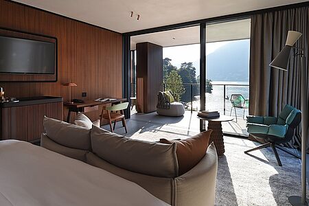Corner Suite (ca. 84 qm) Die Corner Suiten eröffnen einen imposanten Ausblick auf den ruhigen See und die Berge. Große Panoramafenster und edles Interieur bringen die Schönheit der Natur in die Suiten. Große Außenterrassen, gemütliche Möbel, ein großer Esstisch und ein separater Wohnbereich vervollständigen das künstlerische Design.