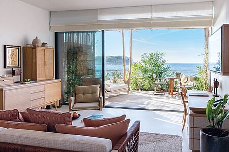 Deluxe Bedroom Ein Zufluchtsort mit raffinierten und modernen Annehmlichkeiten. Ein integrierter Schlafbereich ergänzt den zeitgenössischen Stil, mit großen Fenstern, die den Blick auf Sonnenuntergang und das Meer freigeben.