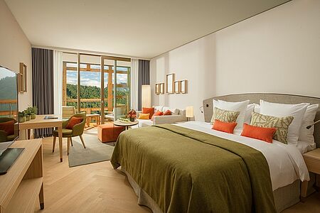 Deluxe Zimmer mit Balkon (40qm) Schlafzimmer mit Kingsize-Bett und Sofa
Badezimmer mit Glaswand, Badewanne
und separater Regendusche