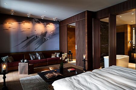 Deluxe Zimmer (ca. 52-55 qm) Die Deluxe Zimmer verfügen über ein komfortables Schlafzimmer und über ein luxuriöses Badezimmer mit großer Badewanne sowie mit Regendusche. Hier treffen Naturstein, poliertes Holz und geschmeidiges Leder aufeinander und verschmelzen zu einem wunderschönen Ambiente. Dank der großen Panoramafenster genießen Sie traumhafte Ausblicke auf die umliegende Landschaft.